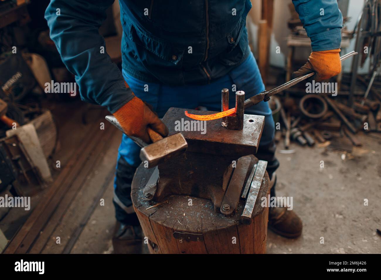 Herrero forja y hace detalles de metal con martillo y yunque en fragua