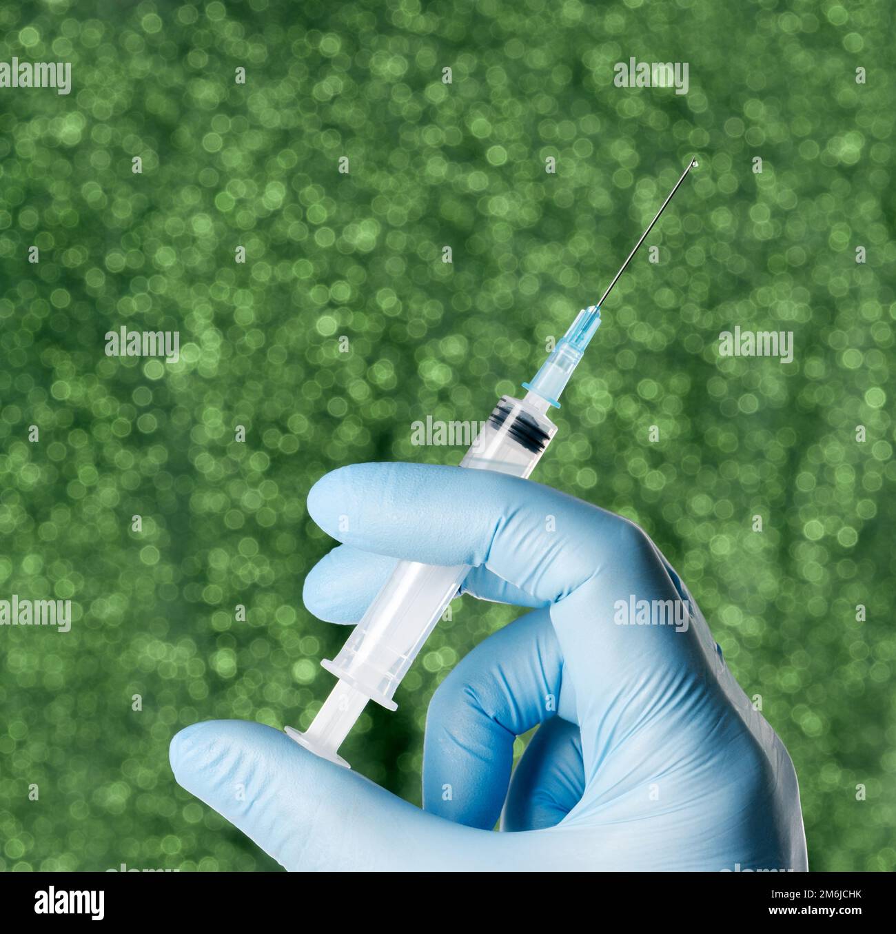 Mano con guante azul sosteniendo una jeringa de fondo verde Foto de stock