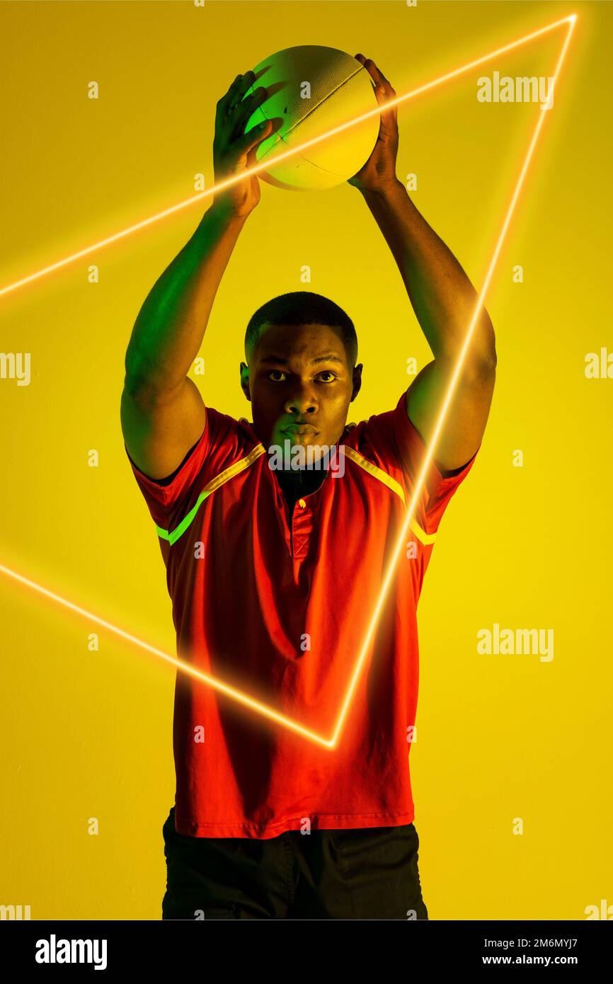 Jugador de rugby masculino afroamericano que lanza la bola sobre el triángulo  iluminado sobre fondo amarillo Fotografía de stock - Alamy