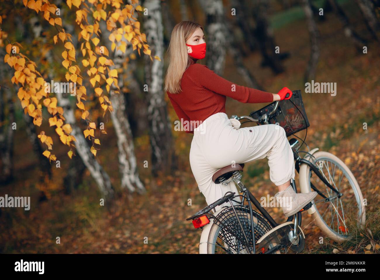 Mujer joven montando en bicicleta con guantes rojos y máscara facial en el  parque de otoño Fotografía de stock - Alamy