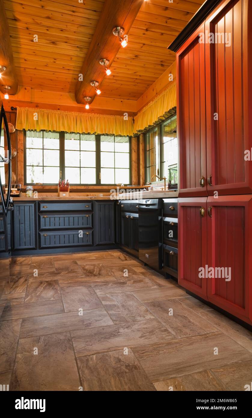 Armarios de madera de carbón rojo y negro en la cocina con piso de cerámica de bronceado dentro de la casa de madera. Foto de stock