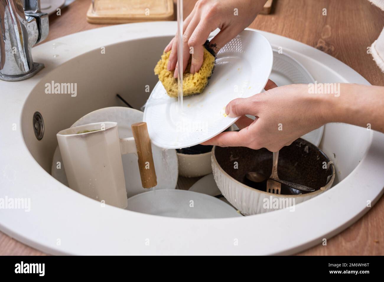 Las manos de las mujeres lavan el plato bajo el agua del grifo. Platos sucios en el fregadero en la cocina, desorden afte Foto de stock