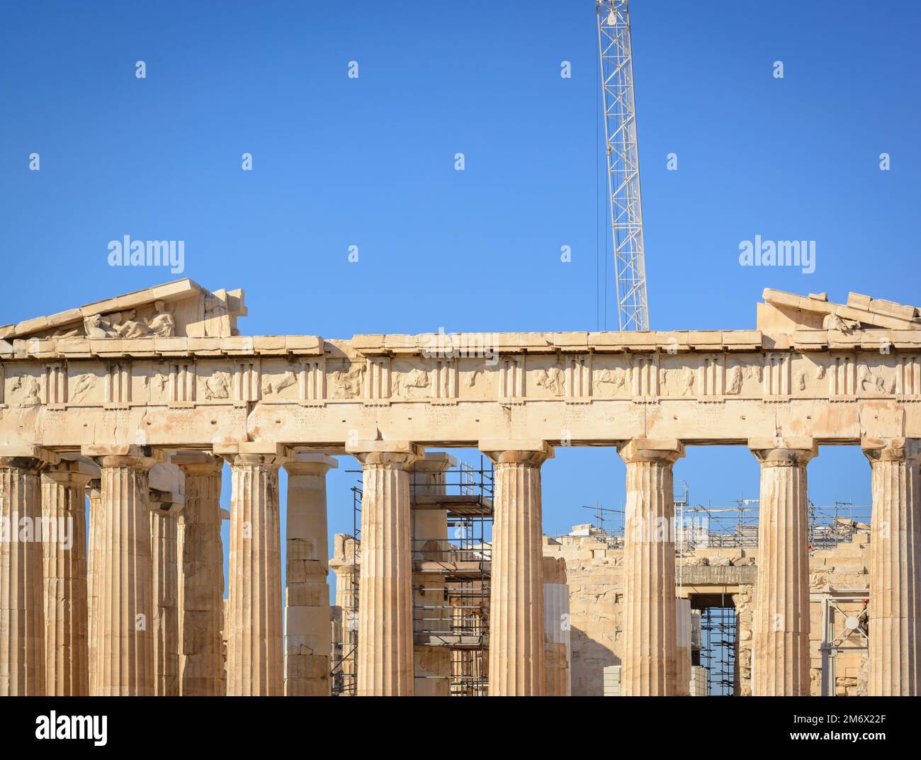 Vista de parte de las columnas dóricas de la Acrópolis y la grúa contra el cielo azul en Atenas Foto de stock