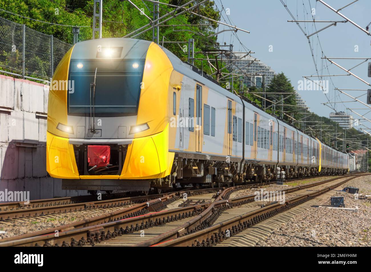 El tren eléctrico de pasajeros suburbano largo amarillo viaja en el ferrocarril Foto de stock