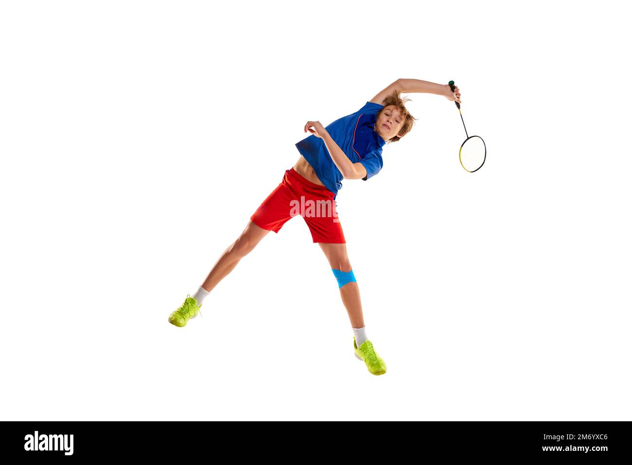 Retrato del muchacho adolescente en uniforme jugando bádminton, entrenamiento aislado sobre fondo blanco. En un salto, sirviendo Foto de stock