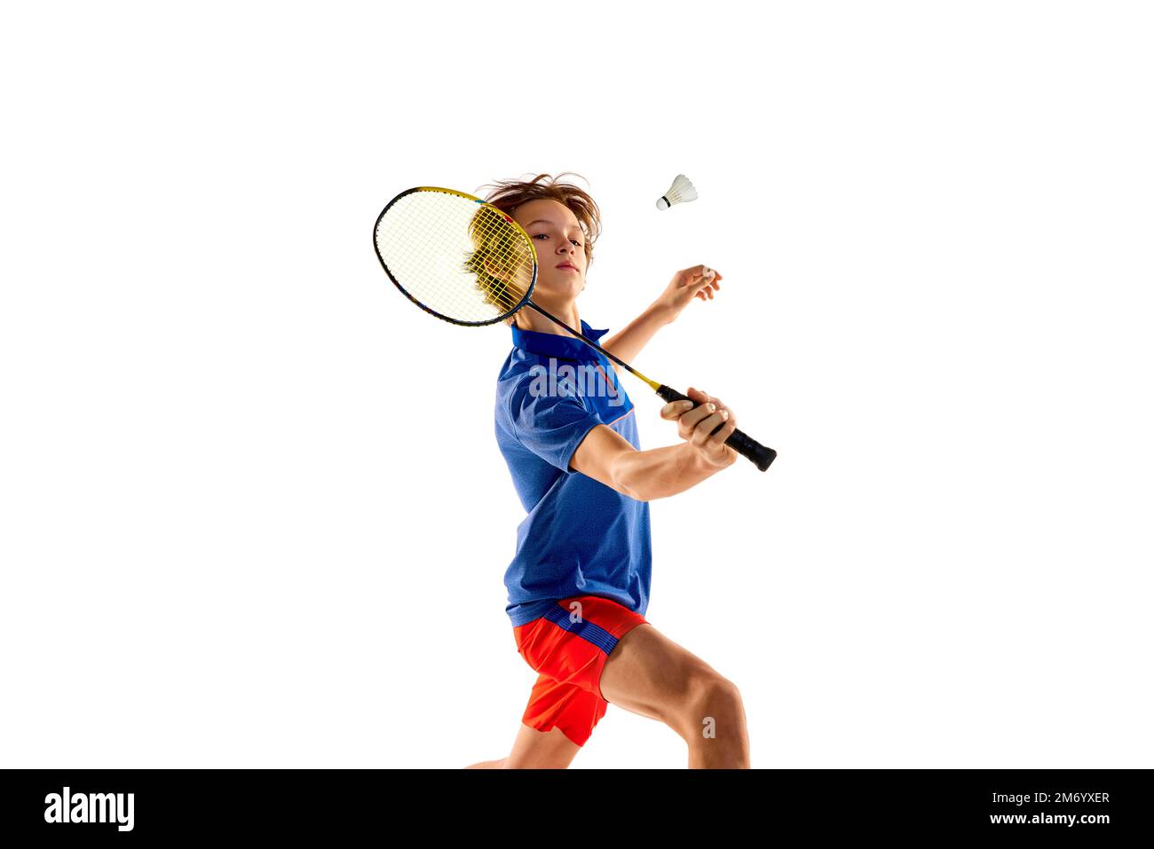 Retrato del muchacho adolescente en uniforme jugando bádminton, entrenamiento shuttlecock que sirve ejercicios aislados sobre fondo blanco Foto de stock