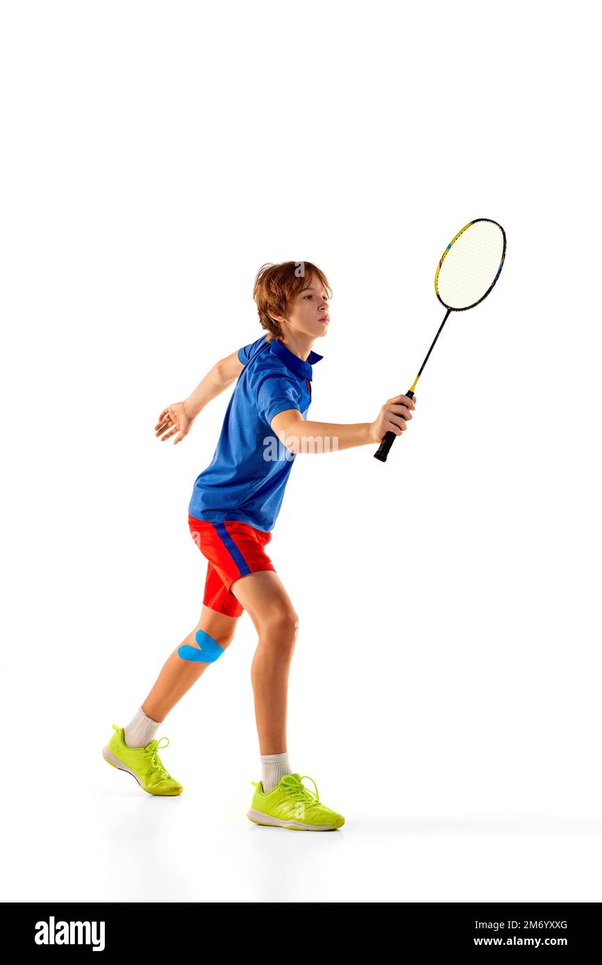 Retrato del muchacho adolescente en uniforme jugando bádminton, entrenamiento, posando con la raqueta aislada sobre fondo blanco. Ganador Foto de stock