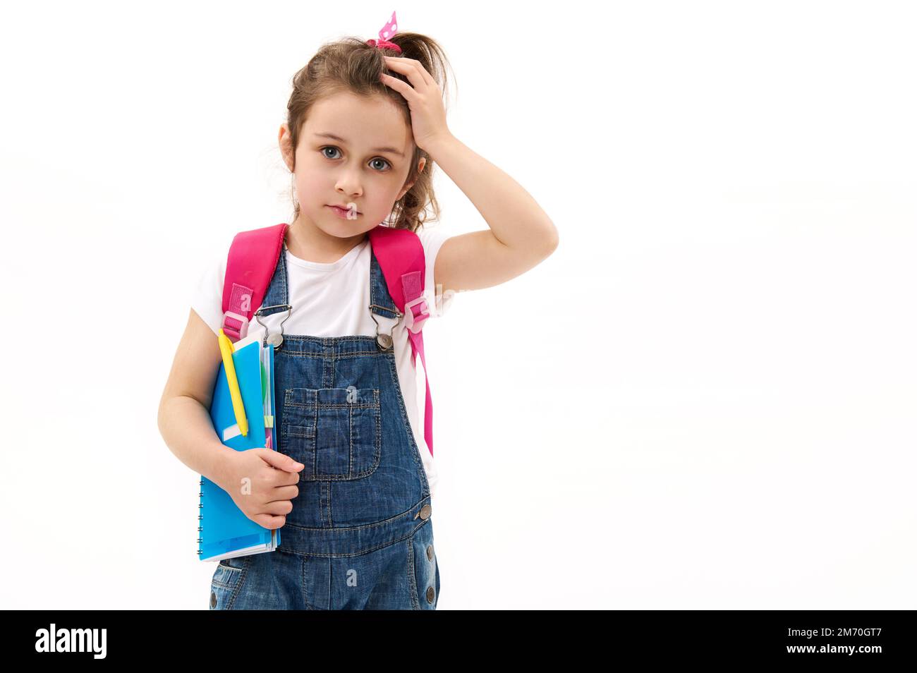 Adorable niña de 5-6 años con mochila rosa, sosteniendo libro de texto y  mostrando el pulgar hacia arriba mirando a la cámara. Maqueta Fotografía de  stock - Alamy