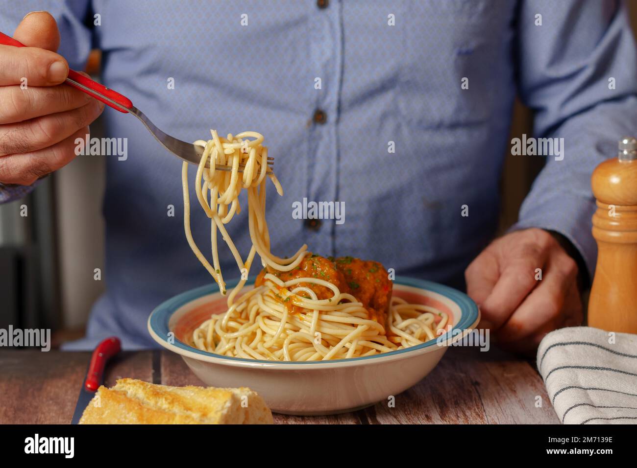 Hombre irreconocible en camisa azul con tenedor comiendo albóndigas con espaguetis Foto de stock