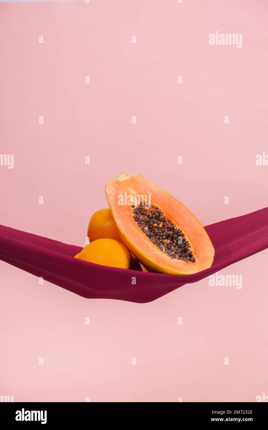 dos naranjas y una papaya cortadas por la mitad sobre un paño rojo delante de un fondo de melocotón como símbolo del suelo pélvico, no hay gente Foto de stock