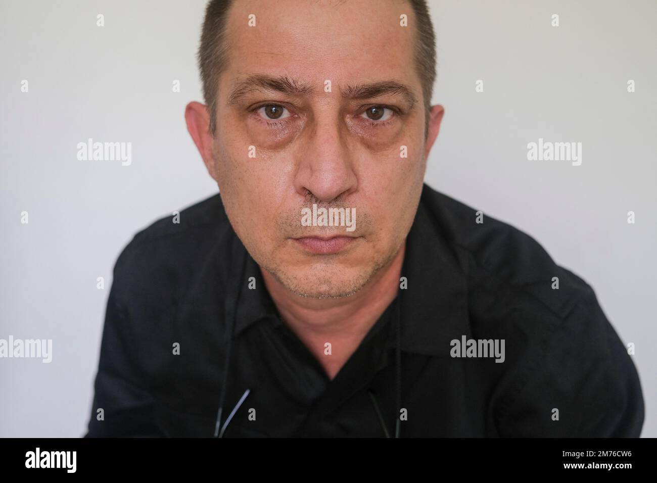 Retrato de primer plano del hombre caucásico con ojos holgados mirando a la cámara, contra bolsas de ojos de fondo blanco Foto de stock