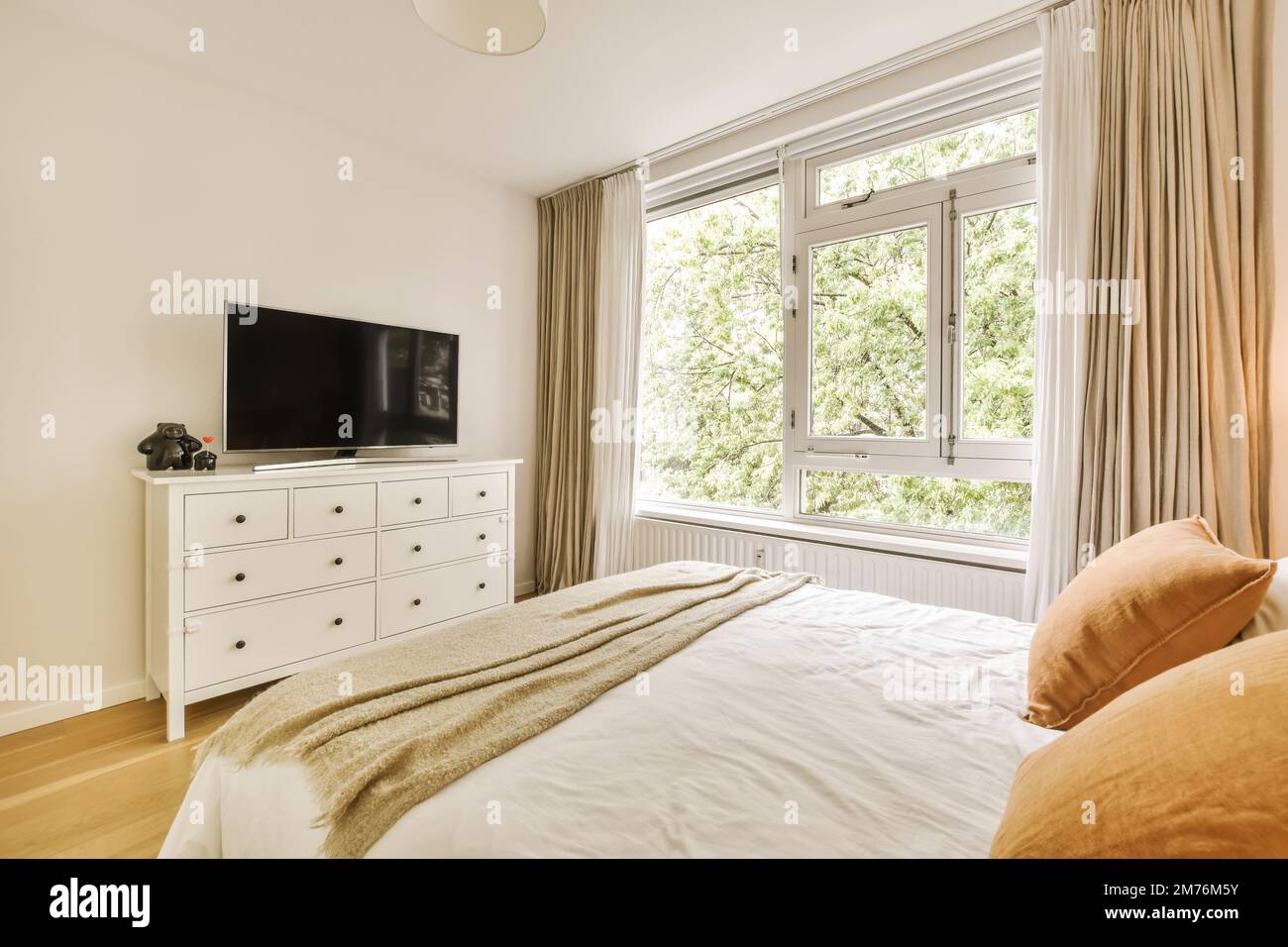 un dormitorio con una cama, tocador y tv en la pared frente a la ventana  con vistas a los árboles fuera Fotografía de stock - Alamy
