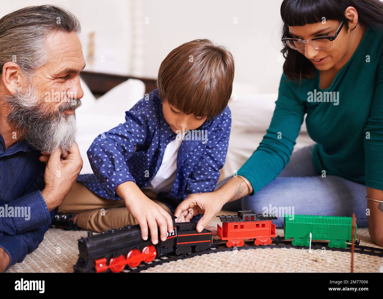 Mostrando a los adultos cómo montar el tren. una madre y un abuelo viendo a un niño jugar con un tren de juguete. Foto de stock