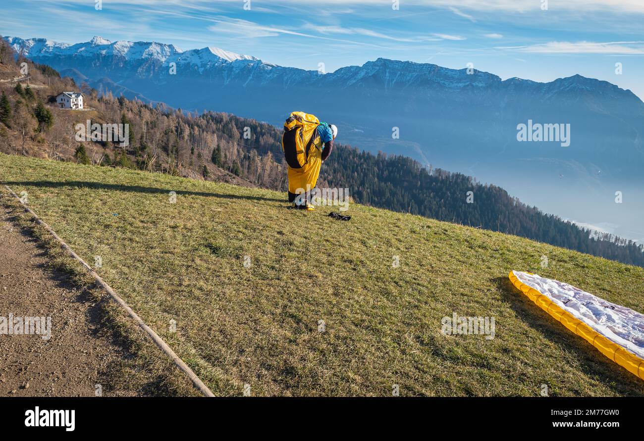 El hombre en una pendiente cubierta de hierba prepara el parapente para el parapente de Vetriolo Terme, provincia de Trento - Trentino Alto Adige - Escuela de parapente - Italia Foto de stock