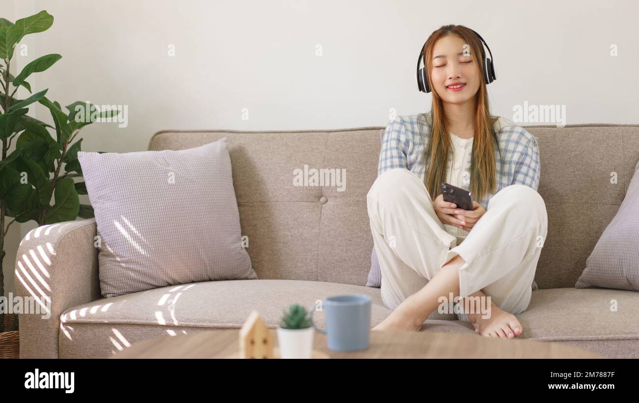 Concepto de tiempo de descanso, mujeres sentadas en el sofá cómodo y usando auriculares para escuchar música. Foto de stock