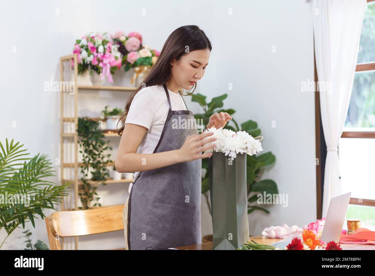 Concepto de florista, florista femenino que arregla el ramo de flores de crisantemo en la bolsa de compras en la tienda. Foto de stock