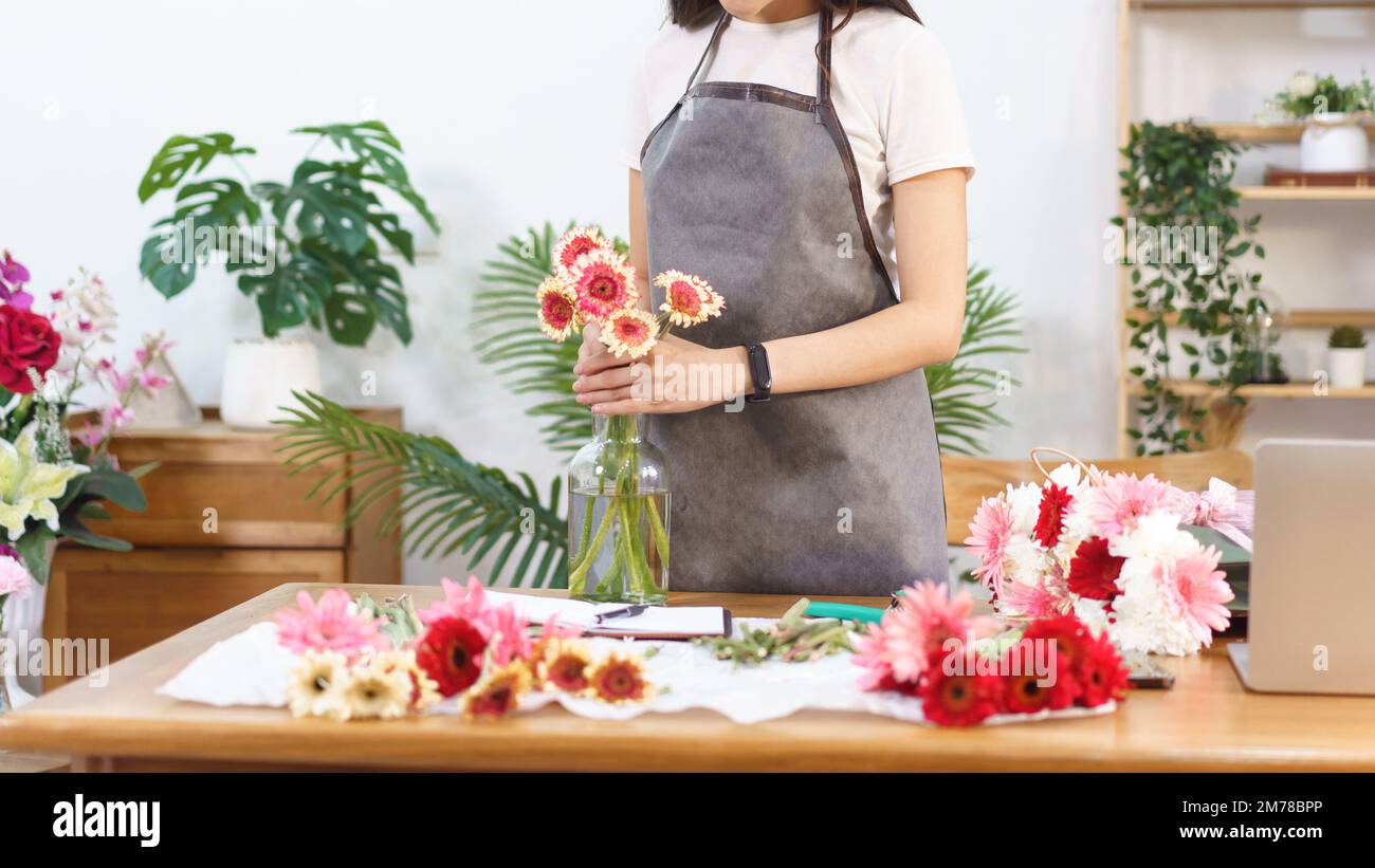 Concepto de floristería, florista femenino que arregla gerbera colorida en jarrón sobre la mesa con felicidad. Foto de stock