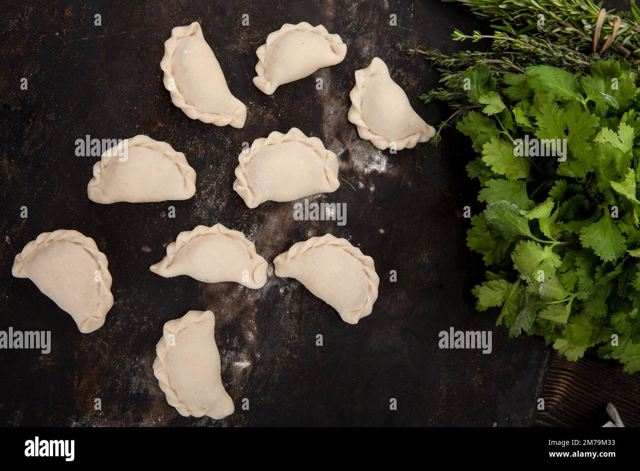 Empanadillas hechas a mano caseras sobre un fondo rústico junto con hierbas Foto de stock