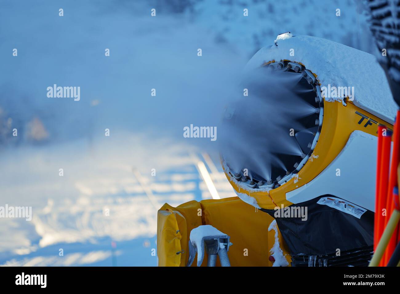 Cañón de nieve en las montañas de invierno. Pistola de nieve rociando cristales de hielo artificiales. Máquina haciendo nieve Foto de stock