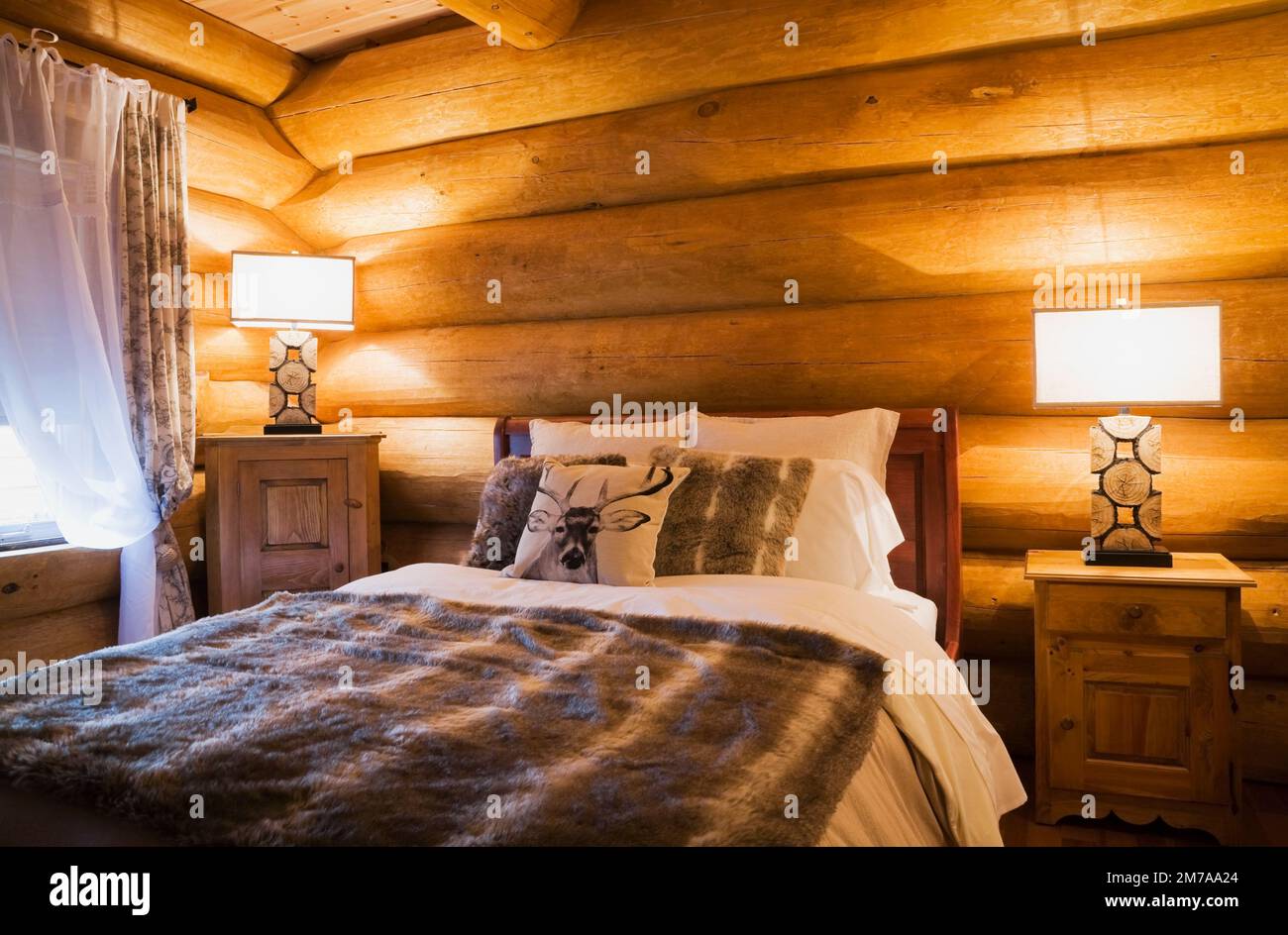 Cama queen size y mesitas de noche de madera con lámparas iluminadas en el dormitorio de invitados en la planta baja dentro de la lujosa casa de madera escandinava. Foto de stock