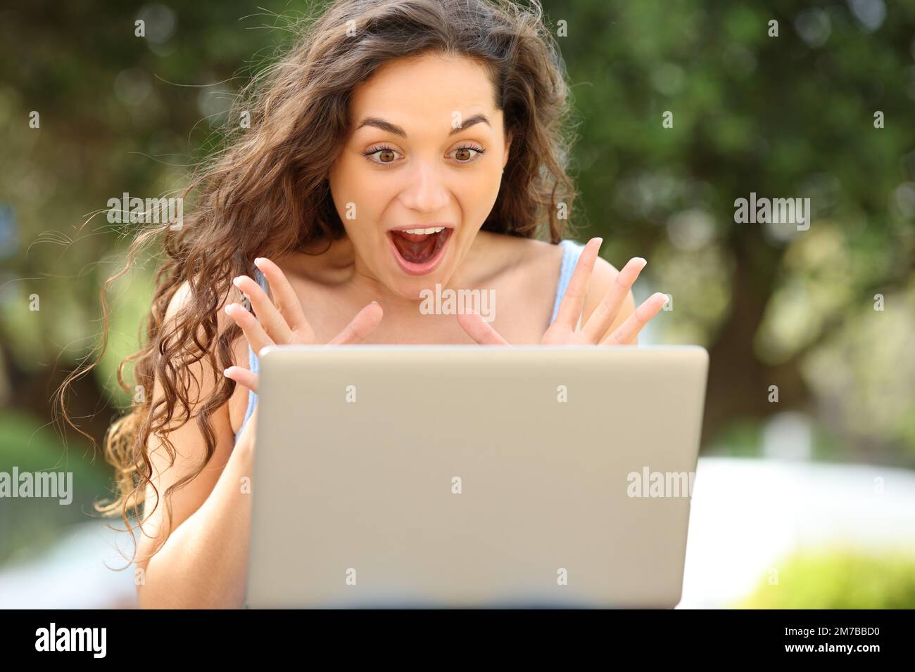 Retrato de la vista frontal de una mujer asombrada que comprueba el ordenador portátil en un parque Foto de stock