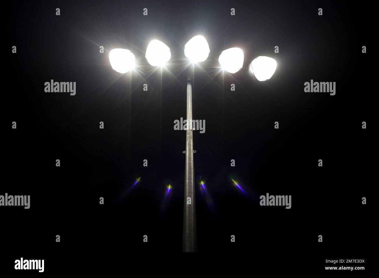 Partido de fútbol local por la noche con un pequeño conjunto de luces de inundación que brillan en la oscuridad. Foto de stock