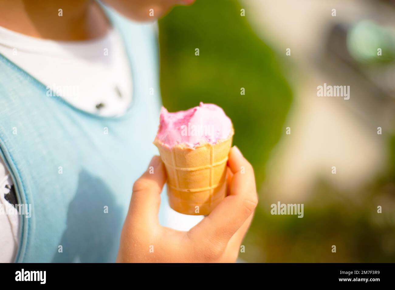 Helado rosa en una taza de gofres, mordido y derretido en las manos de un niño. Foto de stock