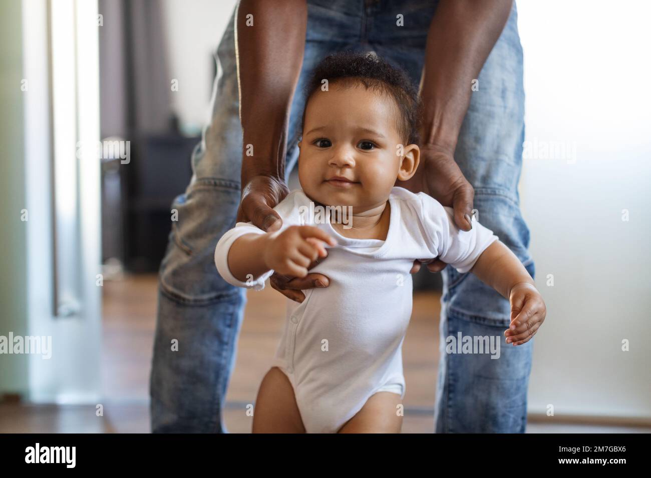 Primer plano del niño infantil negro adorable caminando con la ayuda del padre en la habitación Foto de stock