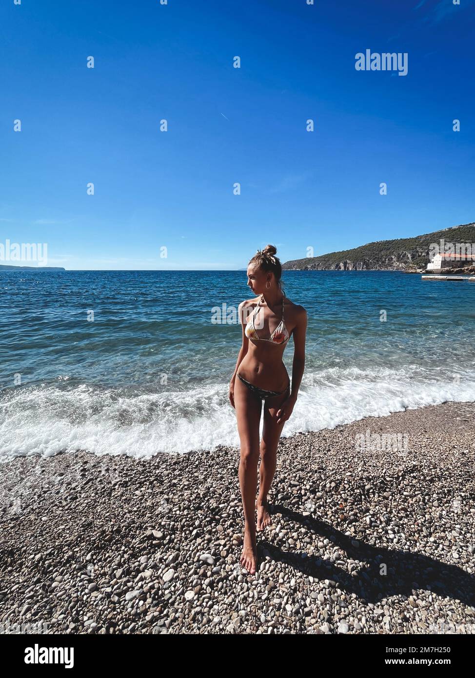 Hermosa modelo alta en traje de baño en la costa rocosa contra el fondo del mar y las islas distantes. Foto de stock