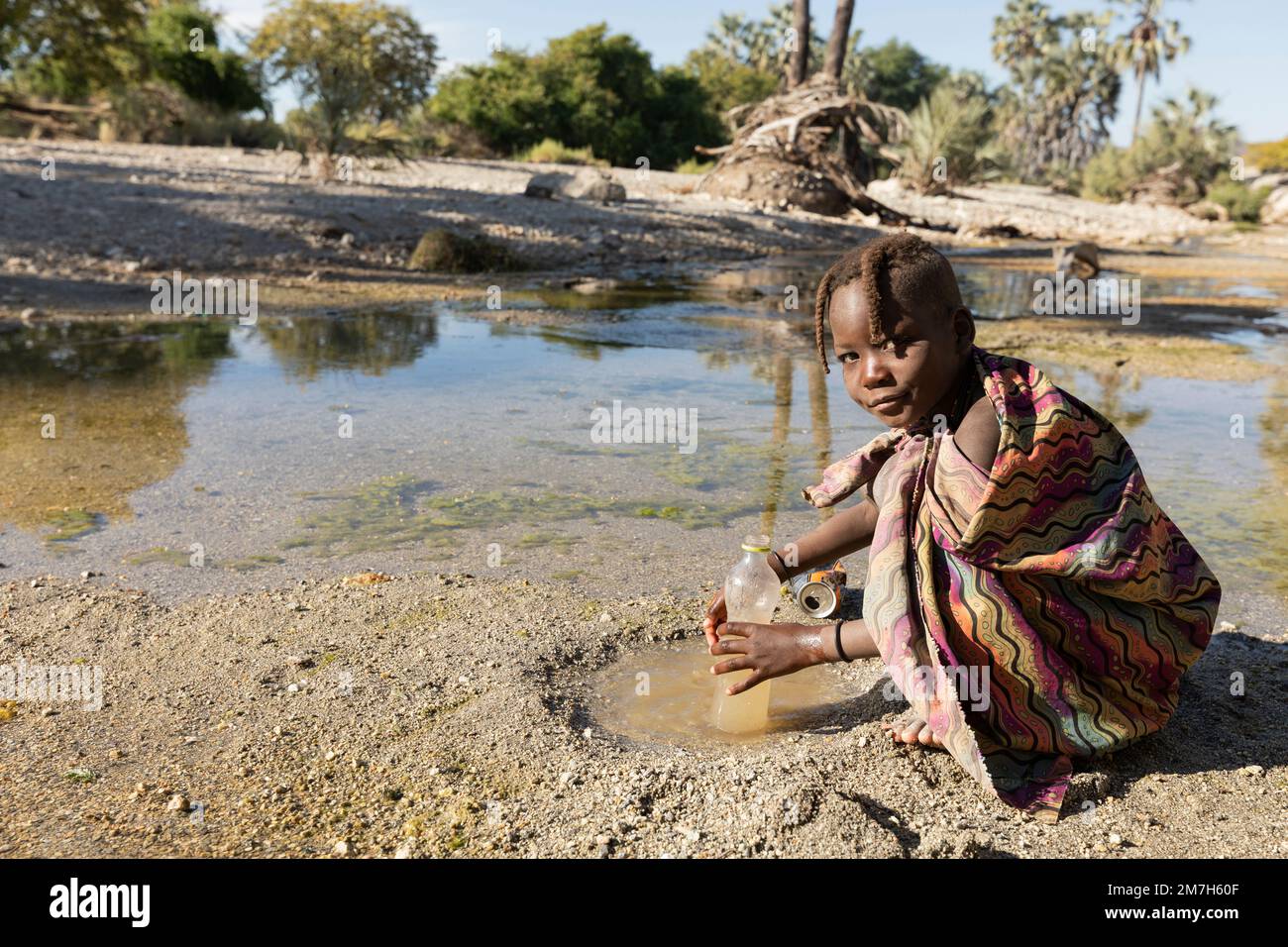 Joven Himba llenando una botella de agua en el río Kunene, Epupa, Namibia Foto de stock
