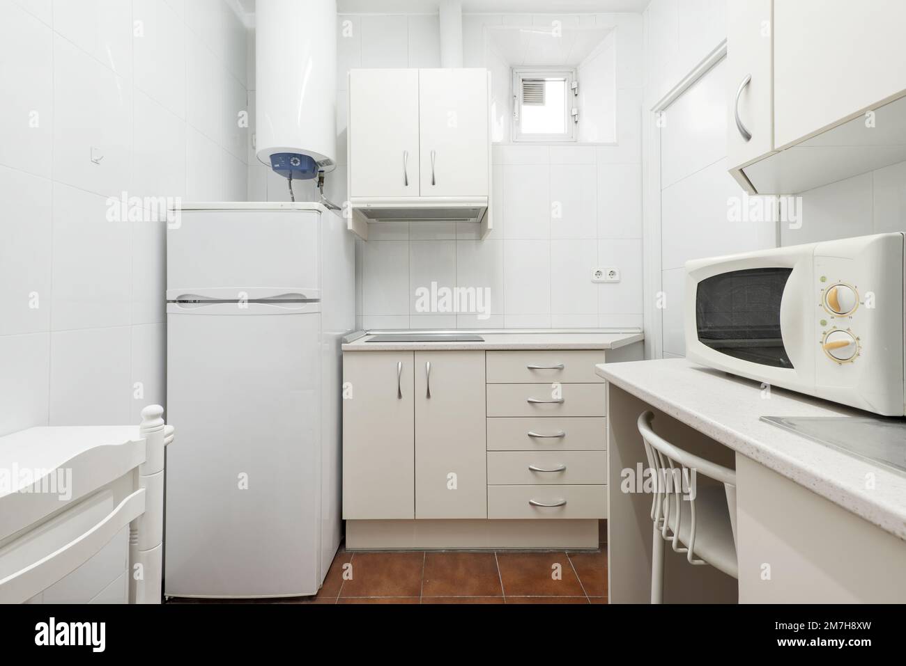 Pequeña cocina con armarios blancos con calentador de agua, nevera blanca y  horno microondas Fotografía de stock - Alamy