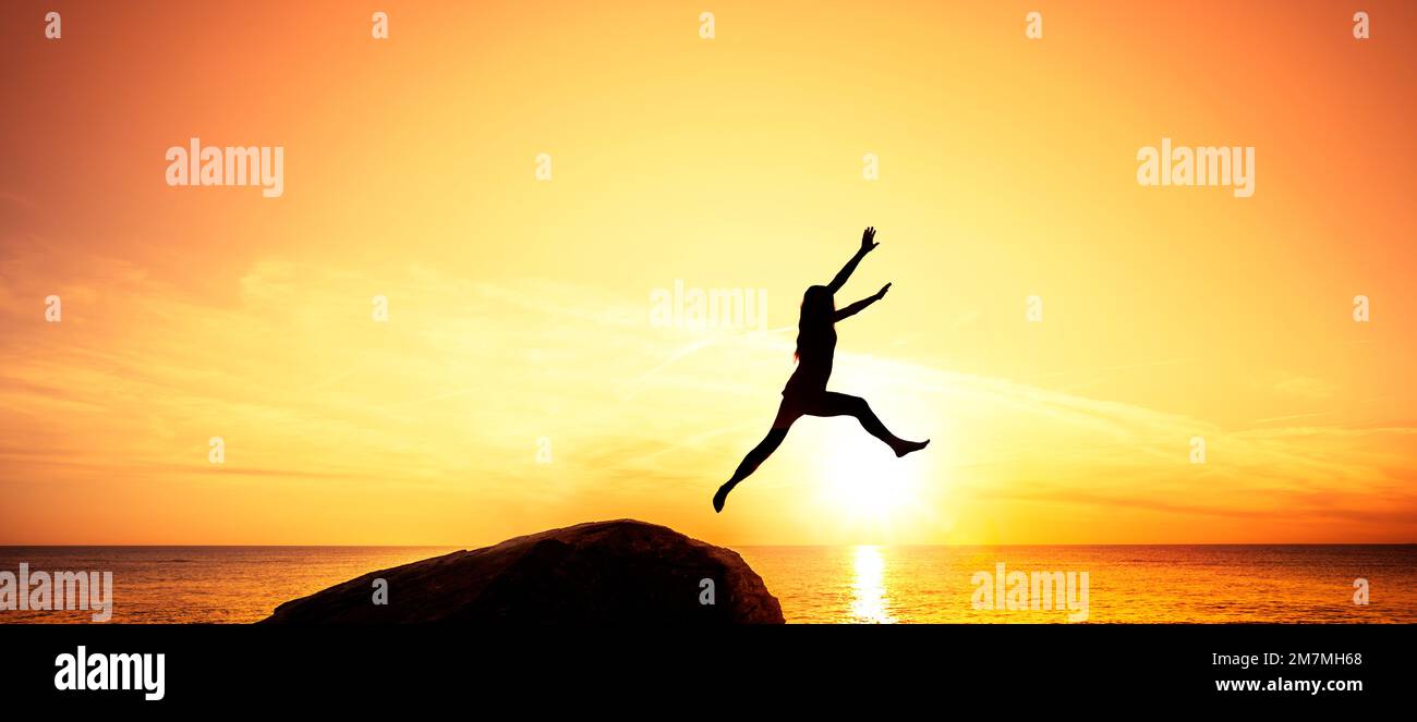 Silueta de mujer saltando sobre el acantilado Foto de stock