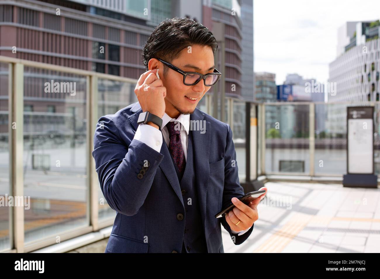 Un joven empresario en la ciudad, en movimiento, un hombre con un traje afuera, sosteniendo un móvil y su oreja, usando auriculares. Foto de stock