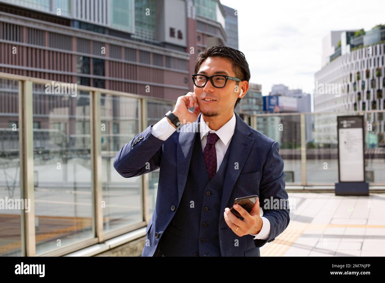 Un joven hombre de negocios en la ciudad, en movimiento, un hombre con un traje, sosteniendo un teléfono móvil y usando un teléfono en la oreja. Foto de stock