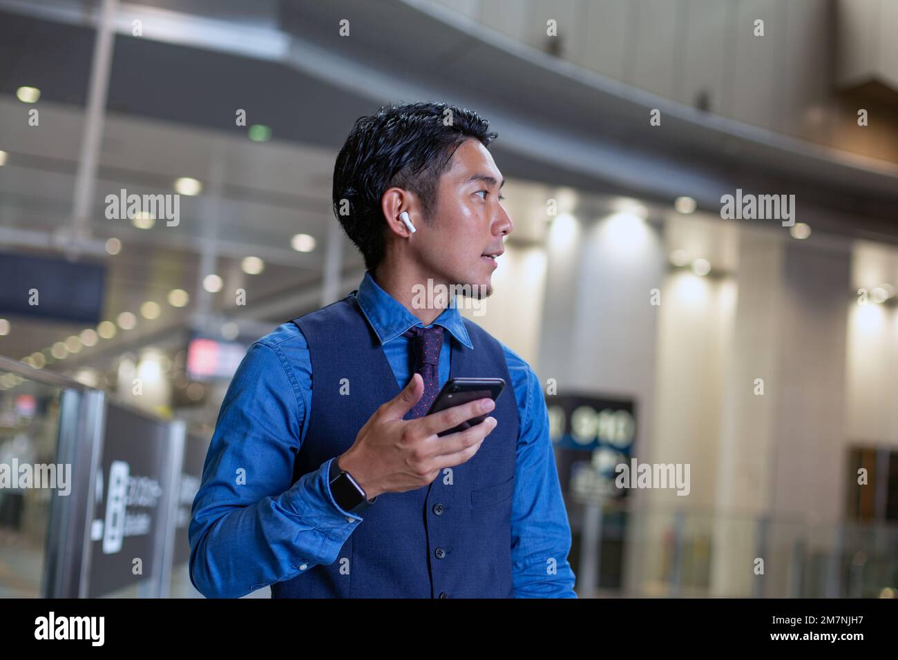 Un joven empresario en la ciudad, en movimiento, en un centro de transporte, sosteniendo su teléfono y mirando a su alrededor. Foto de stock