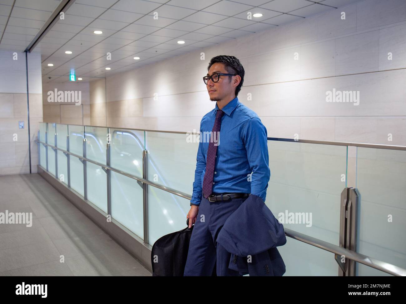 Un joven hombre de negocios en la ciudad, en movimiento, de pie sosteniendo una bolsa de ordenador portátil y un abrigo. Foto de stock