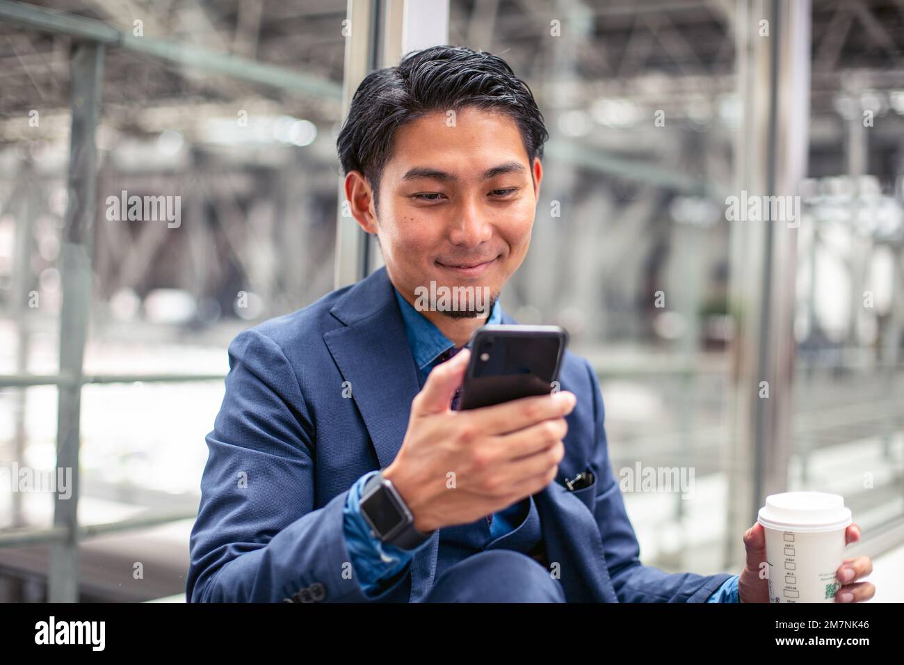 Un joven hombre de negocios con un traje azul en una ciudad, mirando la pantalla de su teléfono móvil, enviando mensajes de texto o leyendo un mensaje. Foto de stock
