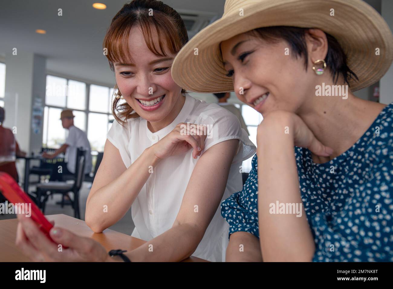 Dos mujeres japonesas maduras, amigas al lado del otro, sentadas mirando la pantalla de un teléfono móvil. Foto de stock