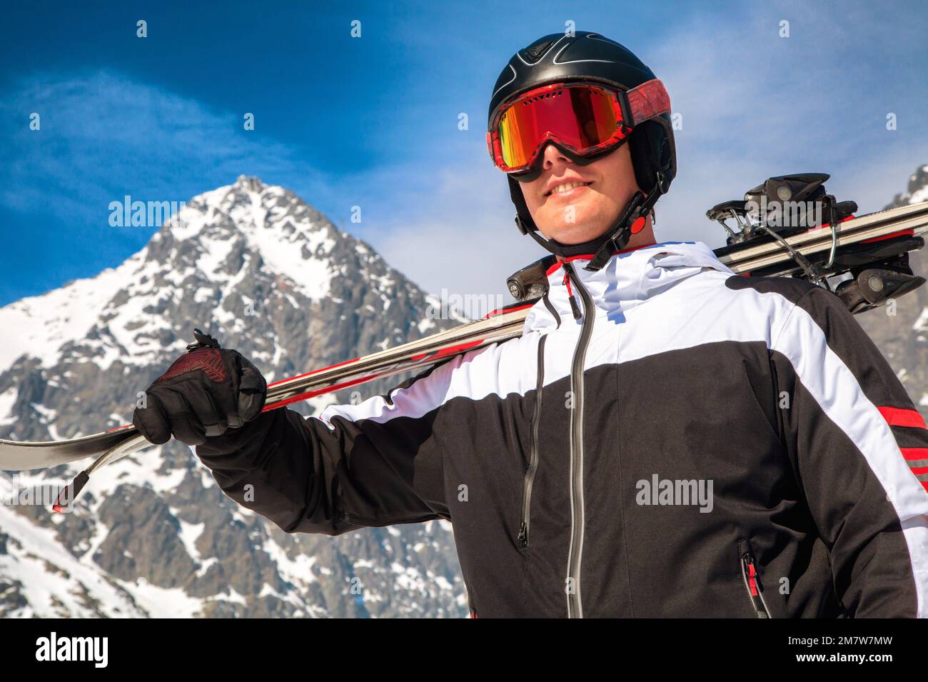 Esquiador masculino con gafas de esquí, casco y esquís posando frente al pico Lomnicky en las montañas de High Tatras Foto de stock