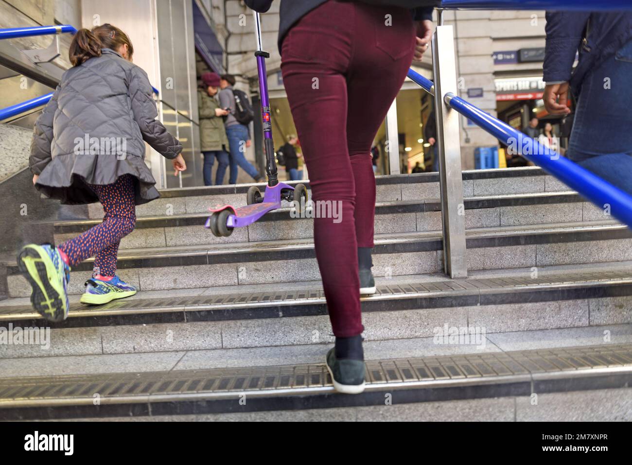 Londres, Inglaterra, Reino Unido. Chica joven con su madre y scooter púrpura - subiendo los pasos de la estación de metro Victoria Foto de stock