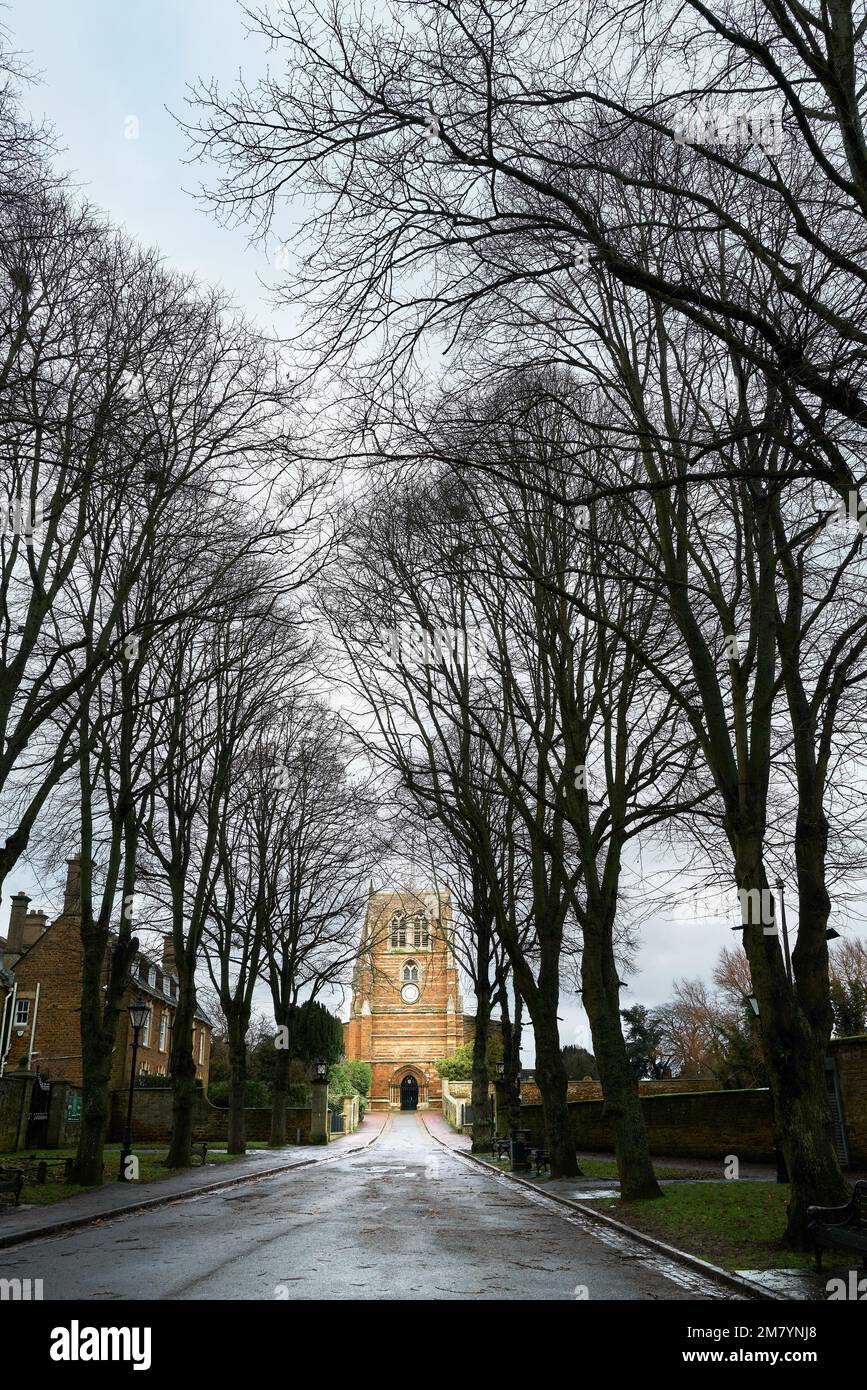 Camino bordeado de árboles a la iglesia cristiana de la Santísima Trinidad en Rothwell, Northamptonshire, Inglaterra, en un día de invierno aburrido. Foto de stock