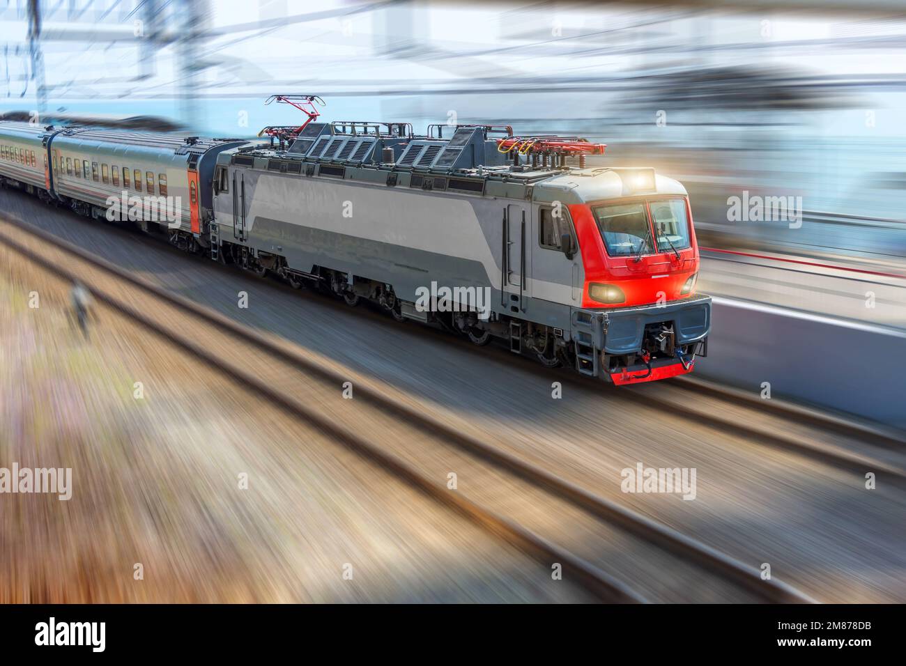 El tren de cabeza de la locomotora eléctrica viaja con un tren de coches de pasajeros con una alta velocidad a lo largo de los carriles Foto de stock