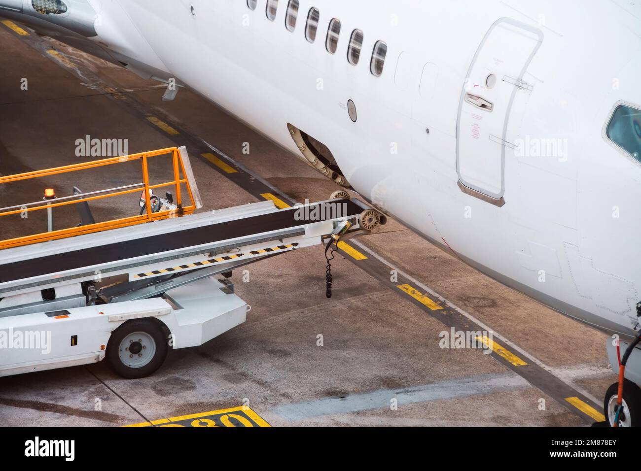 Abra el maletero con equipo de cinta para descargar y cargar el equipaje en un avión de pasajeros Foto de stock