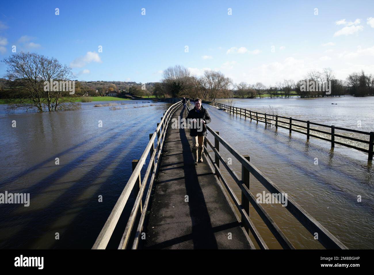 La gente camina a través de un sendero elevado en un puente inundado por el río Avon, en Lacock, Wiltshire. Fecha de la fotografía: Viernes 13 de enero de 2023. Foto de stock