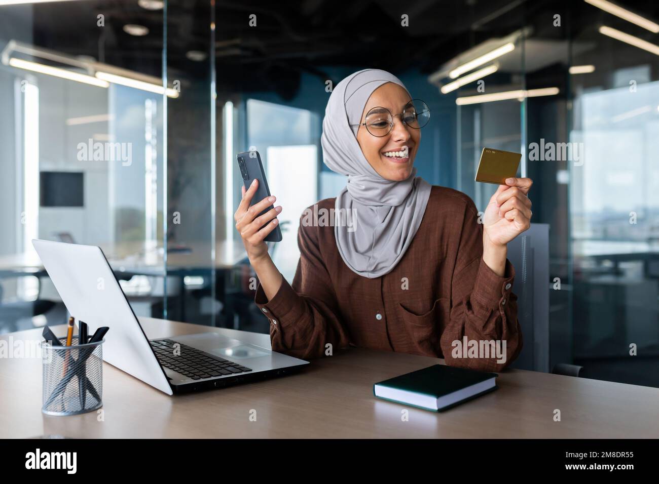 Hermosa Mujer Musulmana Con Ropa Formal Y Hiyab Haciendo Compras En Línea  Con Tarjeta De Crédito Y Teléfono Inteligente. Joven Parada Cerca Del  Edificio De Oficinas Y Disfrutando De Un Pago Fácil.