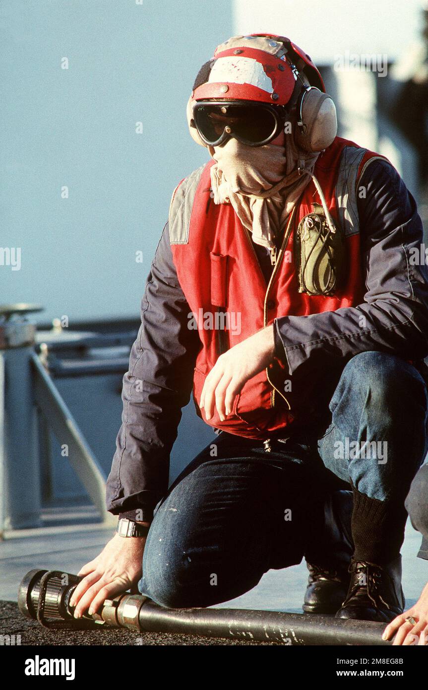 Un tripulante de cubierta de vuelo se encuentra junto a una manguera de  fuego a bordo del buque de mando anfibio USS BLUE RIDGE (LCC-19) como  reposición vertical durante la Operación Tormenta