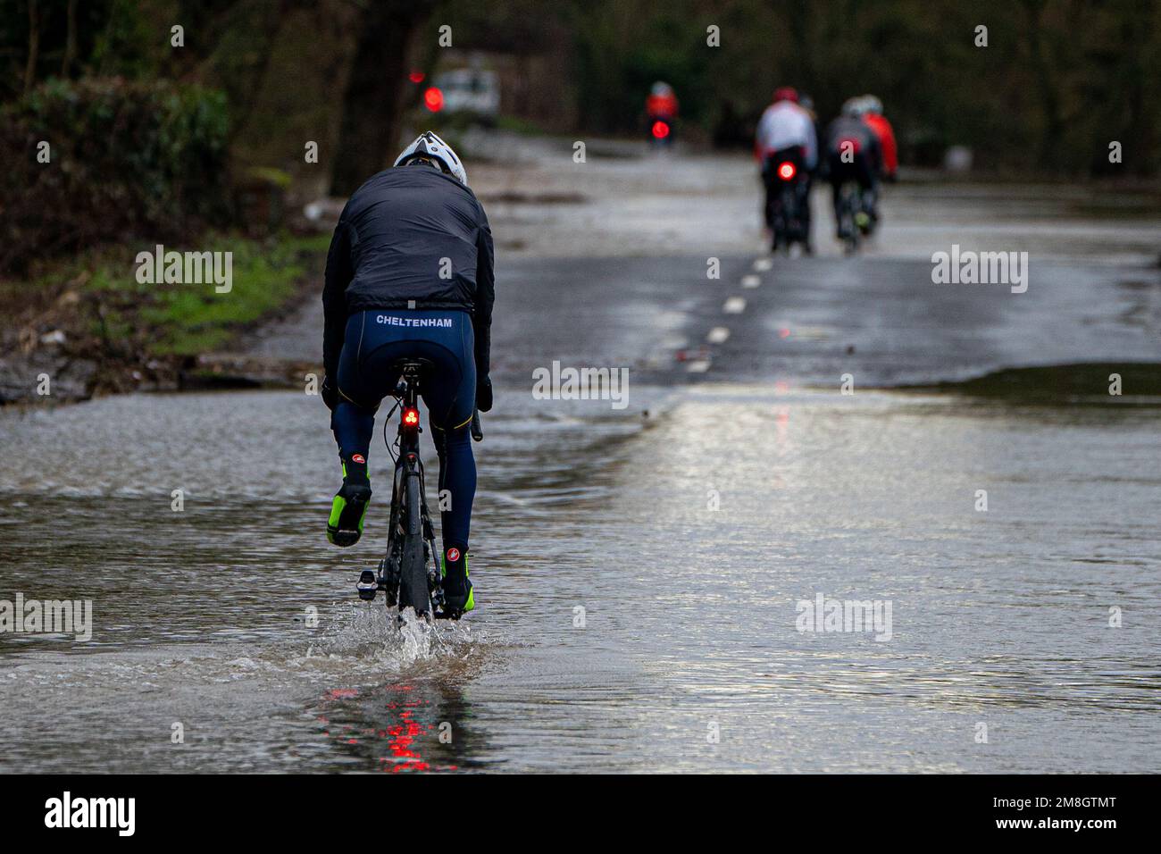 Un ciclista pedalea con un pie mientras recorre las inundaciones en Apperley, Gloucestershire, donde el río Severn irrumpe en sus orillas y ha inundado campos y carreteras en todo el condado. Las fuertes lluvias y los vientos azules en gran parte del Reino Unido este fin de semana serán seguidos por un período de clima frío potencialmente severo la próxima semana. Fecha de la foto: Sábado 14 de enero de 2023. Foto de stock