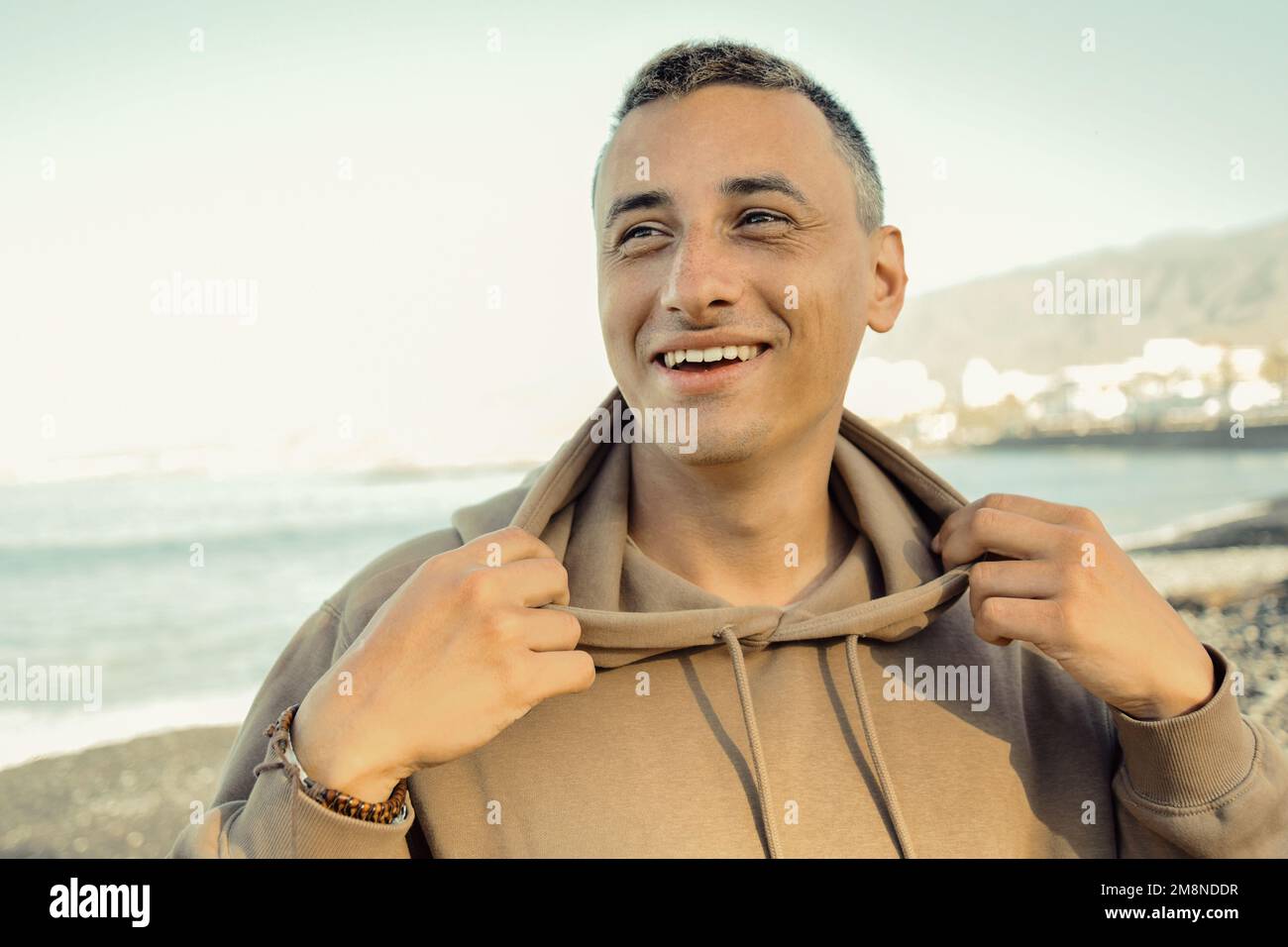 Un hombre una sudadera con capucha contra fondo del mar. Un chico está caminando en la playa y disfrutando de las vistas, la felicidad de viajar en el verano