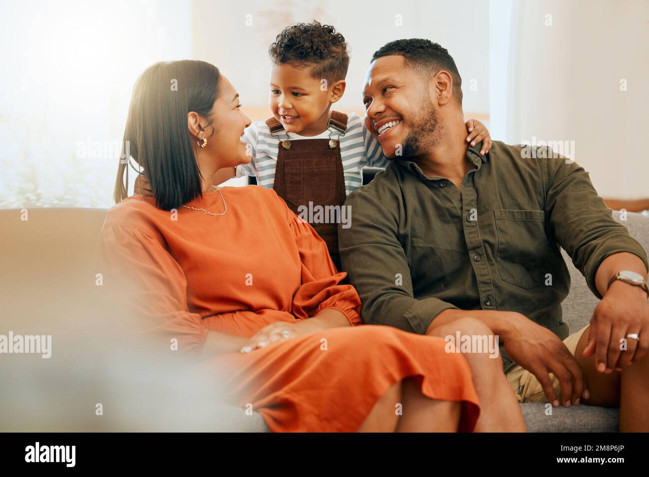 Una feliz familia de tres personas que se relajan juntos en el salón. Cariñosa relación de familia negra con su hijo mientras habla en el sofá en casa Foto de stock