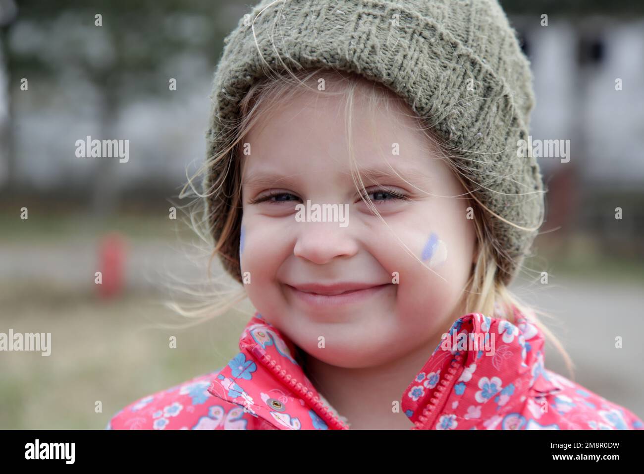 Retrato de niña en edificio arruinado con la bandera de Ucrania pintada en su cara. Refugiados, crisis de guerra, concepto de desastre humanitario. Foto de stock